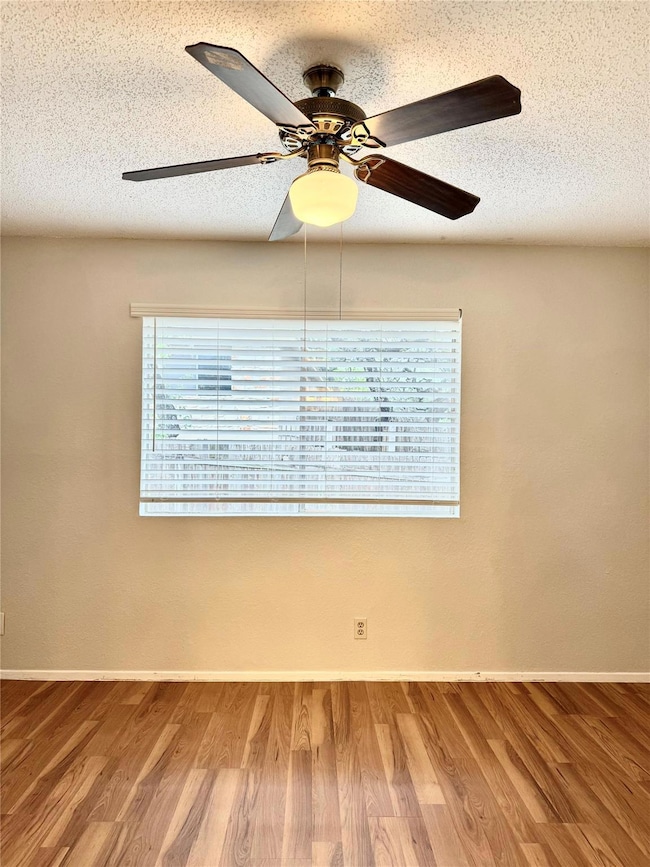 Empty room with a textured ceiling, wood finished floors, plenty of natural light, and ceiling fan