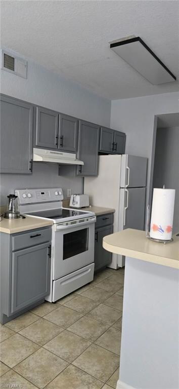 Kitchen with gray cabinets, light countertops, white appliances, under cabinet range hood, and a textured ceiling