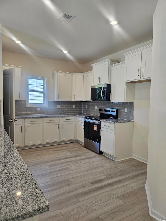 Kitchen featuring white cabinetry, appliances with stainless steel finishes, light stone counters, tasteful backsplash, and LVP flooring  Please note photos are of similar home plan, colors and options vary from home