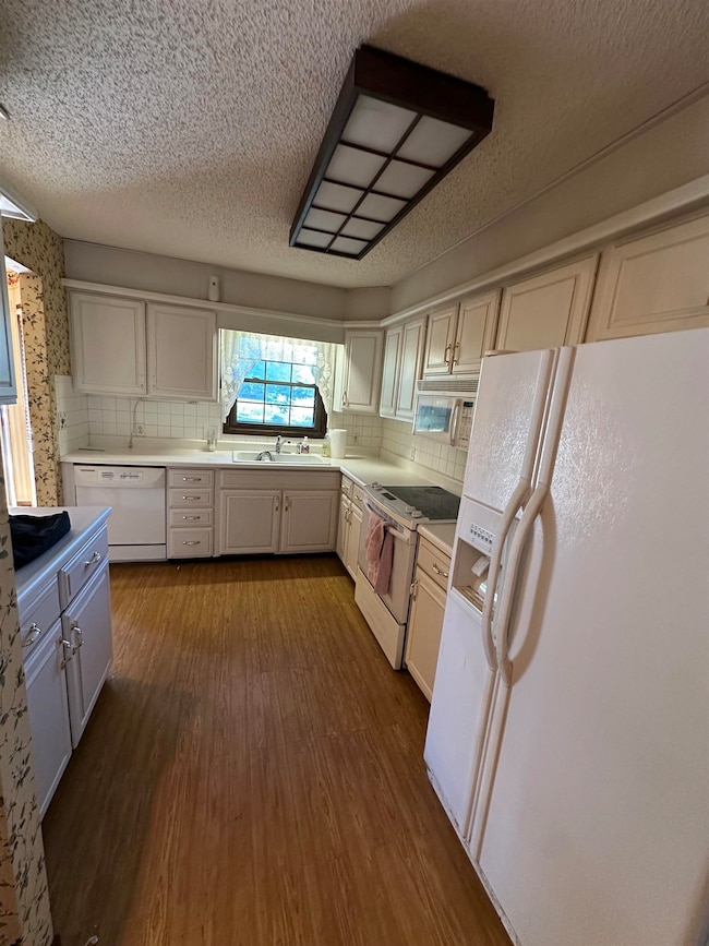 Kitchen featuring white appliances, light countertops, a textured ceiling, dark wood-style floors, and decorative backsplash