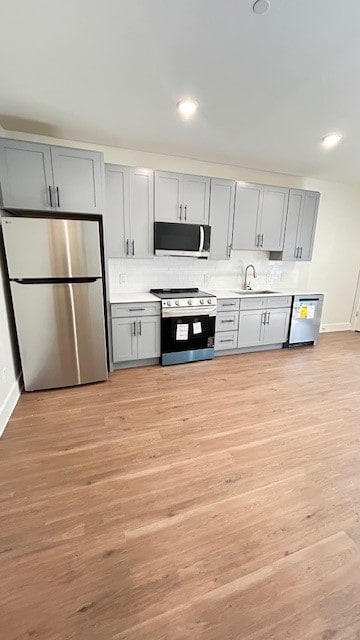 Kitchen featuring stainless steel appliances, gray cabinets, light countertops, light wood-style floors, and recessed lighting