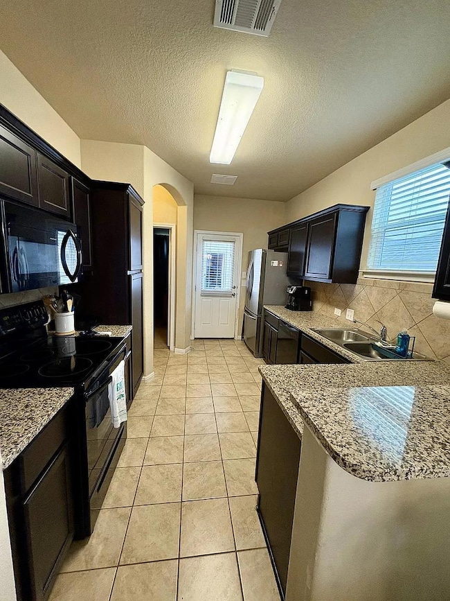 Kitchen featuring backsplash, black appliances, arched walkways, a textured ceiling, and light stone countertops