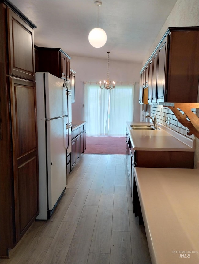Kitchen featuring light countertops, pendant lighting, freestanding refrigerator, dark brown cabinets, and tasteful backsplash