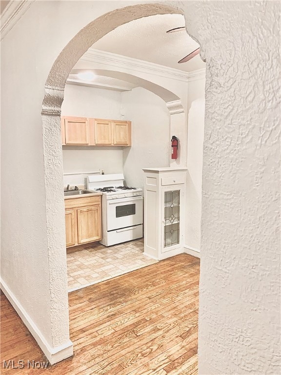 Kitchen with a textured wall, ornamental molding, light brown cabinetry, white range with gas cooktop, and a textured ceiling