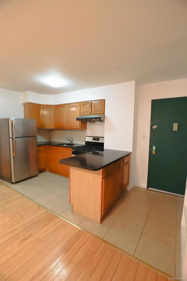 Kitchen featuring appliances with stainless steel finishes, a peninsula, brown cabinets, and light tile patterned flooring