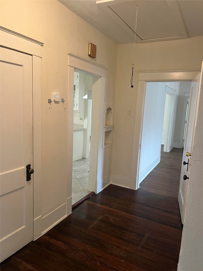 Corridor featuring attic access, dark wood-type flooring, and a textured wall