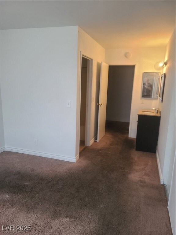 Hallway with a sink, dark carpet, and baseboards