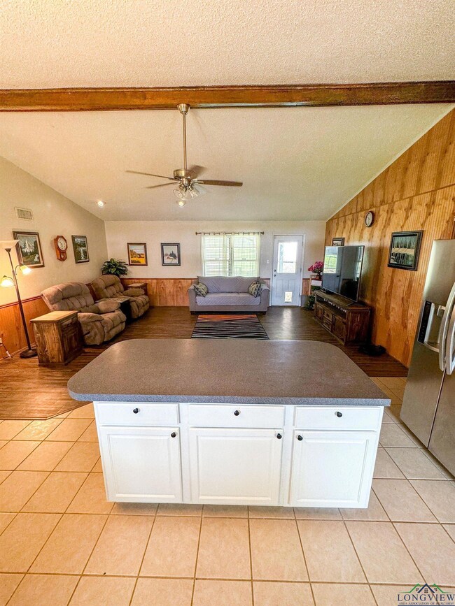 Kitchen with stainless steel fridge with ice dispenser, wooden walls, open floor plan, dark countertops, and a ceiling fan