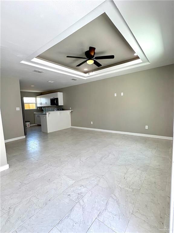 Unfurnished living room with a tray ceiling and ceiling fan