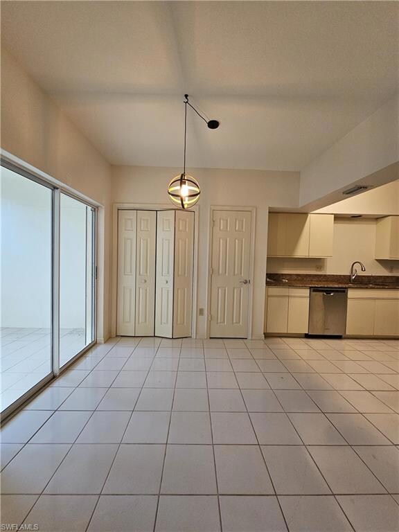 Kitchen featuring stainless steel dishwasher, dark countertops, hanging light fixtures, light tile patterned flooring, and a sink