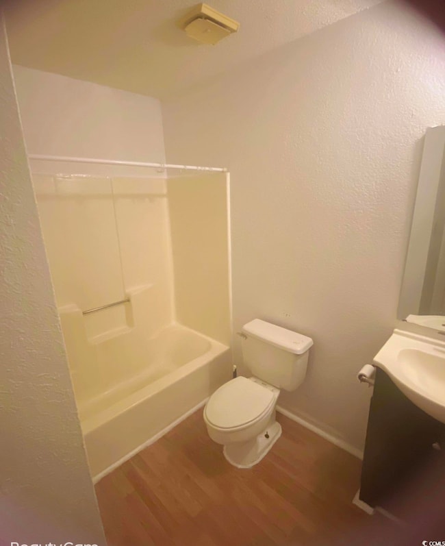 Bathroom featuring wood finished floors, toilet, vanity, shower / washtub combination, and baseboards