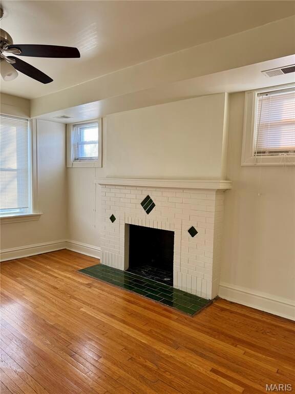 Unfurnished living room with hardwood / wood-style floors, a brick fireplace, and a ceiling fan