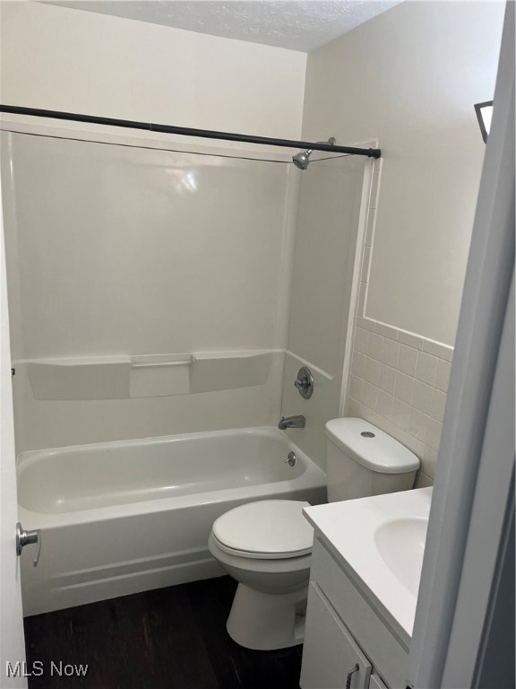 Bathroom with dark wood finished floors, tile walls, vanity, a textured ceiling, and bathing tub / shower combination