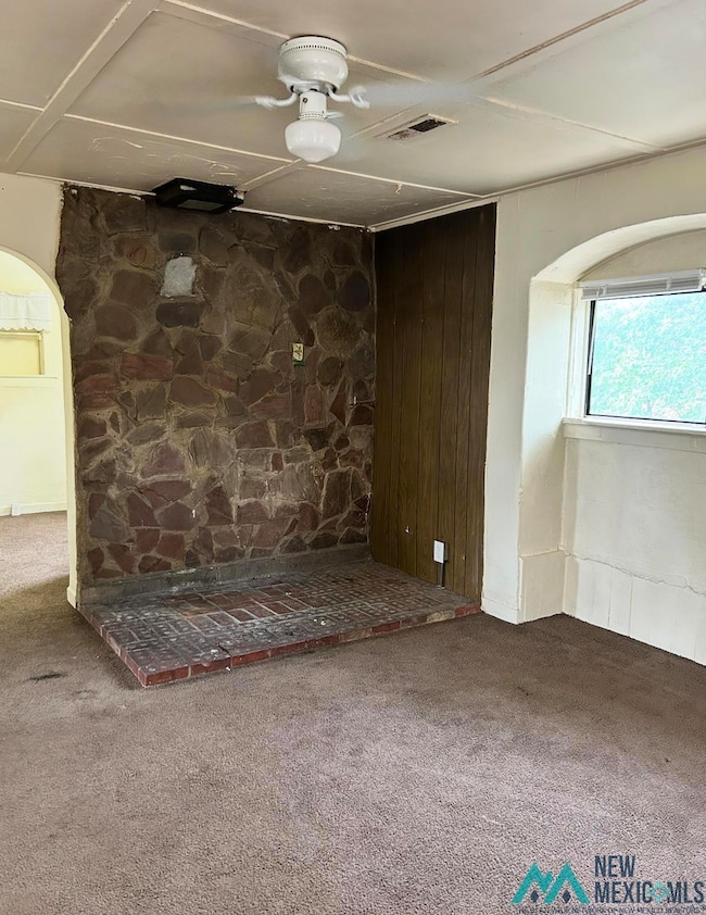 Unfurnished living room featuring arched walkways, carpet, and wooden walls