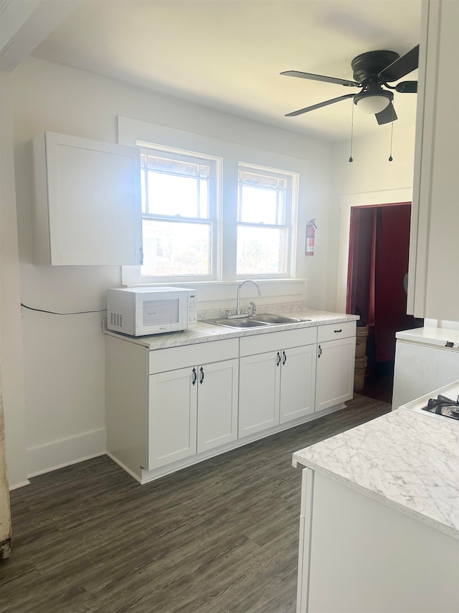 Kitchen with white microwave, a sink, dark wood finished floors, a ceiling fan, and light countertops