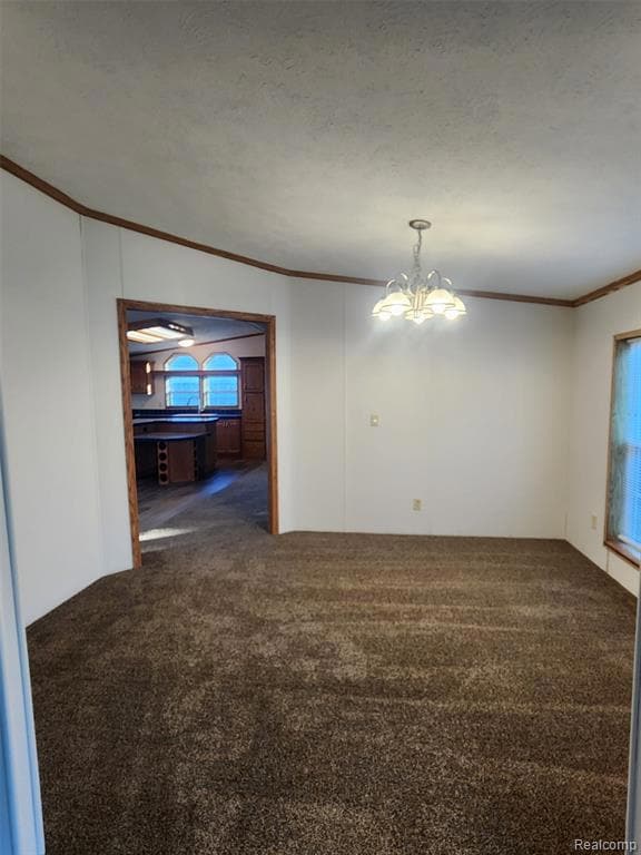 Empty room with crown molding, dark carpet, and a chandelier