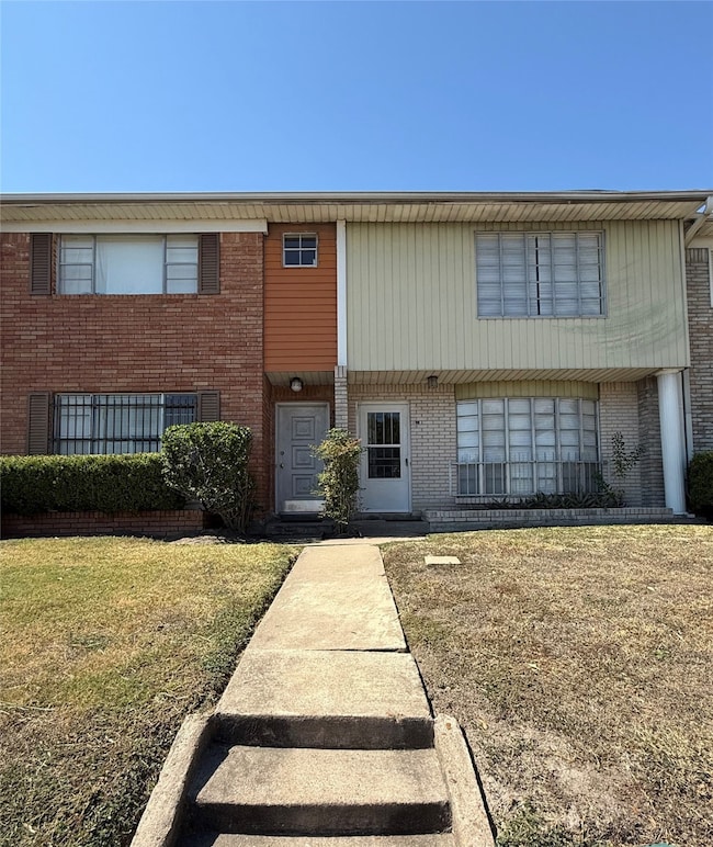 two-story townhouse with a mix of brick and siding exterior. The entrance features a small porch with minimal landscaping. A concrete walkway leads up from the sidewalk. The property has large windows on both floors, providing ample natural light.
