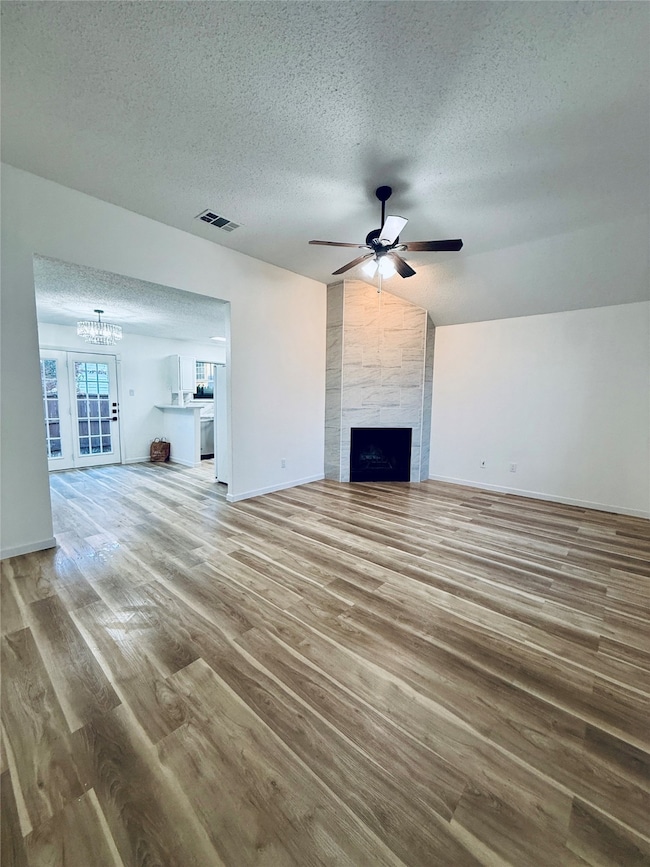 Unfurnished living room with a textured ceiling, lofted ceiling, light wood-type flooring, a tile fireplace, and ceiling fan