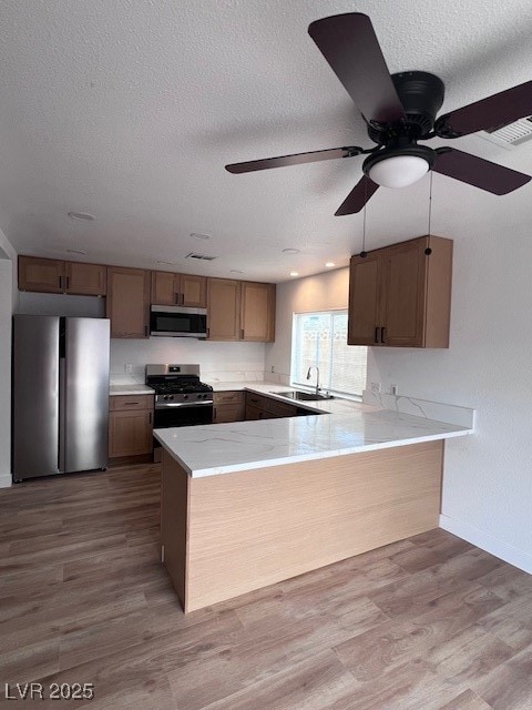 Kitchen with fridge, a peninsula, light wood-style flooring, a textured ceiling, and light stone countertops