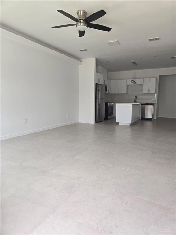 Unfurnished living room featuring ceiling fan and baseboards