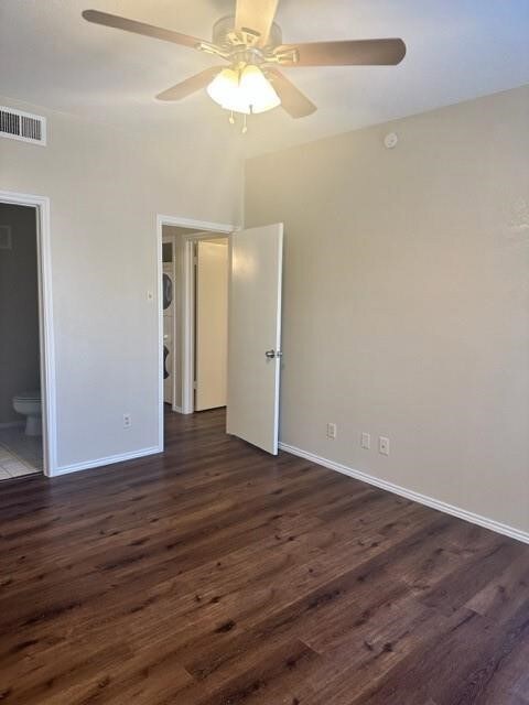 Unfurnished bedroom featuring dark wood-style floors, estacked washer and dryer, a ceiling fan, and ensuite bath