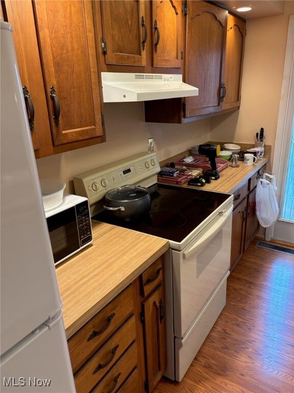 Kitchen with white appliances, light countertops, wood finished floors, under cabinet range hood, and brown cabinets