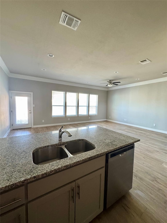 Kitchen with wood finished floors, open floor plan, crown molding, stainless steel dishwasher, and light stone countertops