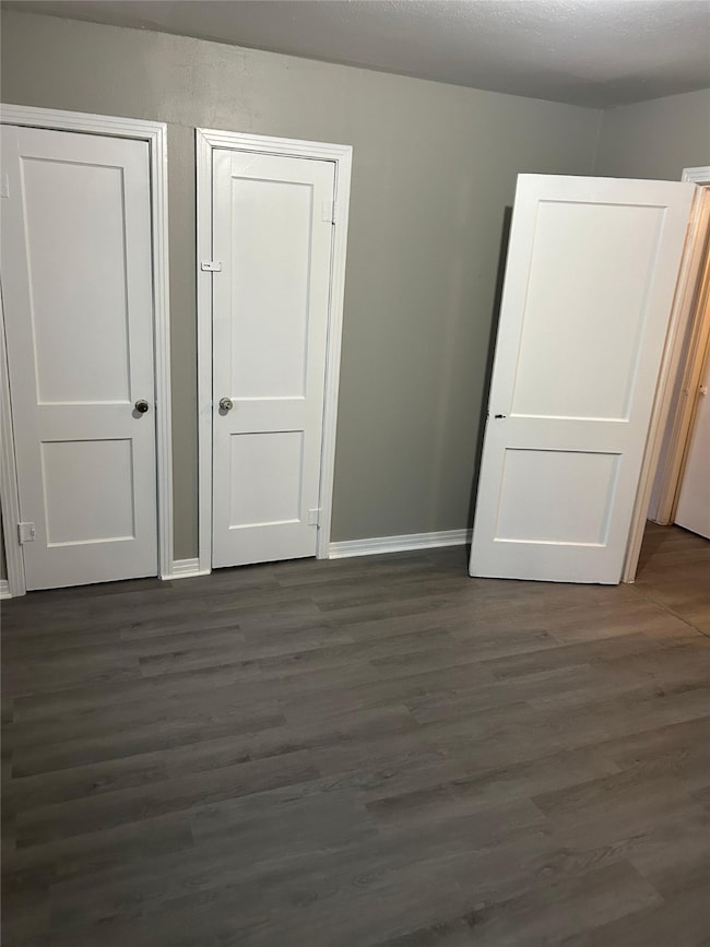 Unfurnished bedroom featuring dark wood-style flooring and baseboards