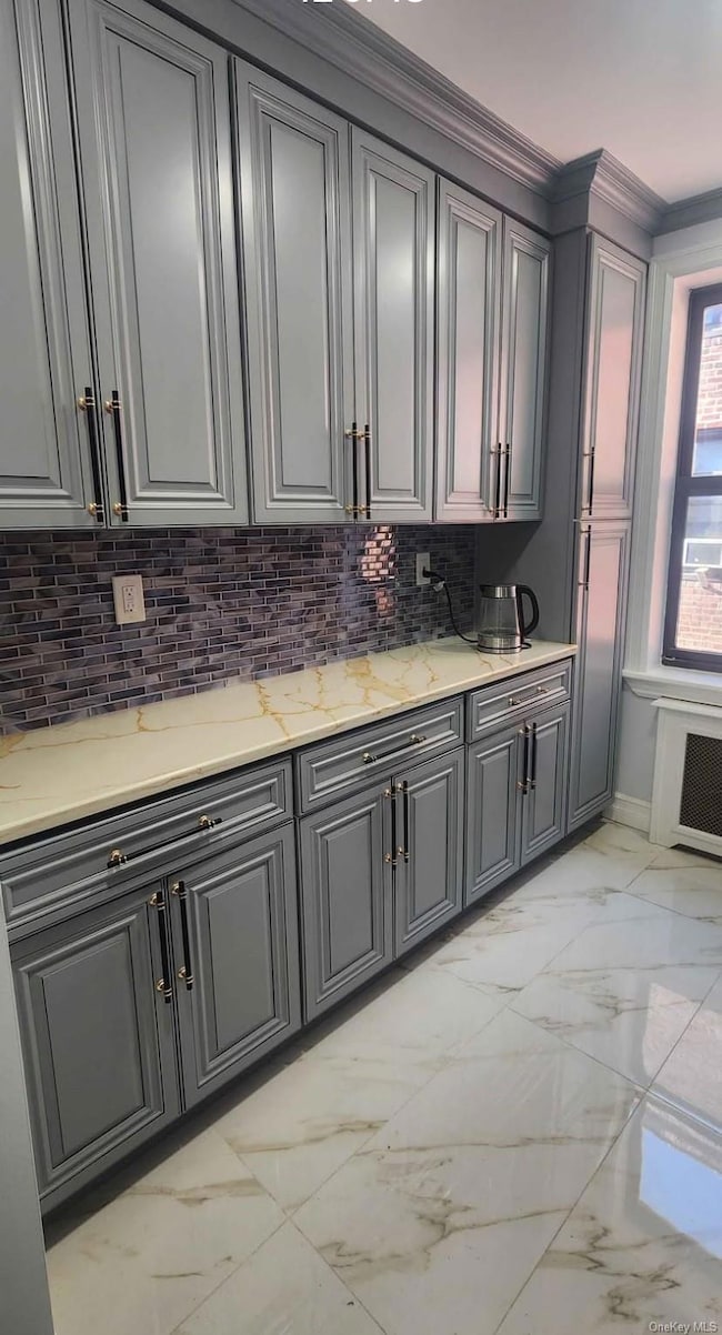 Kitchen featuring light marble finish flooring, gray cabinetry, backsplash, light stone counters, and radiator