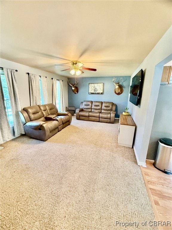 Carpeted living room with ceiling fan and baseboar