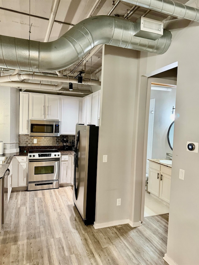 Kitchen featuring stainless steel appliances, light wood-type flooring, tasteful backsplash, and white cabinets