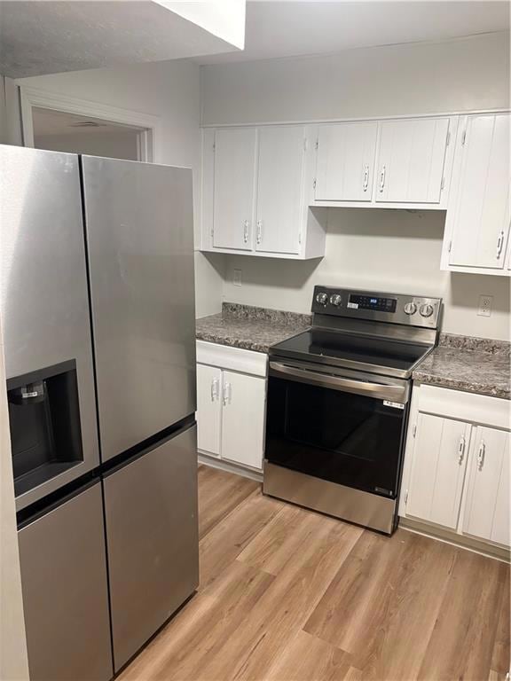Kitchen featuring fridge, stainless steel stove, white cabinets, light wood finished floors, and dark countertops