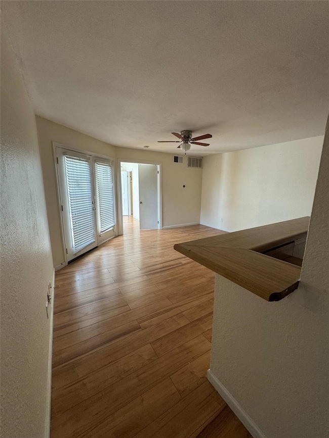 Unfurnished living room featuring light wood-style flooring, a textured wall, a textured ceiling, and a ceiling fan
