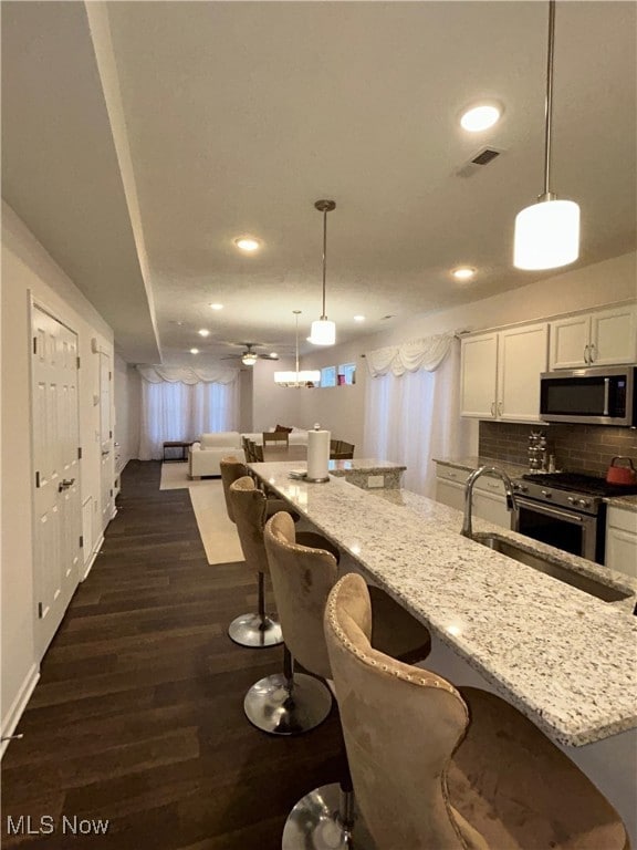 Kitchen with white cabinetry, light stone counters, decorative light fixtures, a breakfast bar area, and recessed lighting