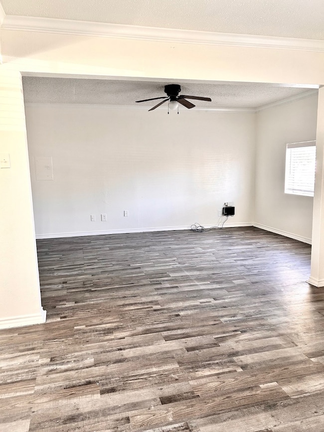 Empty room with wood finished floors, a ceiling fan, ornamental molding, and a textured ceiling