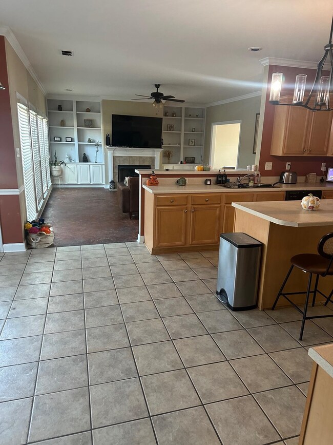 Kitchen with ornamental molding, a breakfast bar area, light countertops, light tile patterned floors, and a tiled fireplace