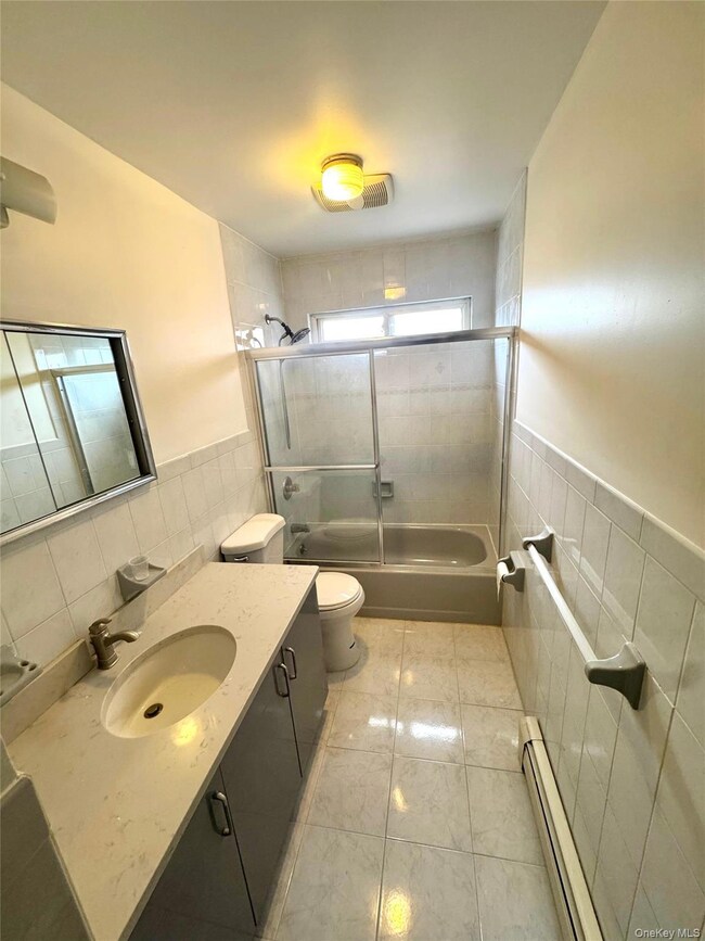 Bathroom featuring tile walls, a wainscoted wall, vanity, a baseboard heating unit, and bath / shower combo with glass door