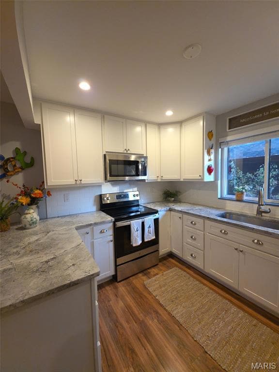 Kitchen with stainless steel appliances, white cabinetry, light stone counters, dark wood-style flooring, and backsplash