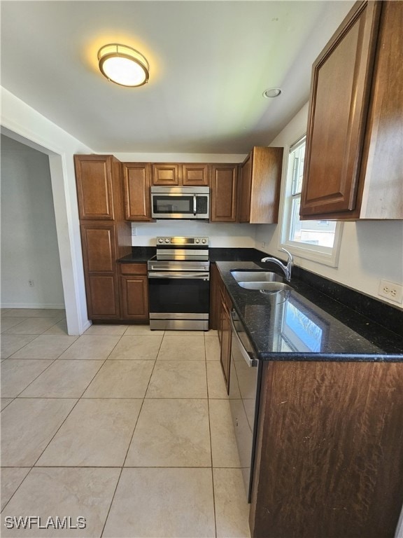 Kitchen with stainless steel appliances, light tile patterned floors, and dark stone counters