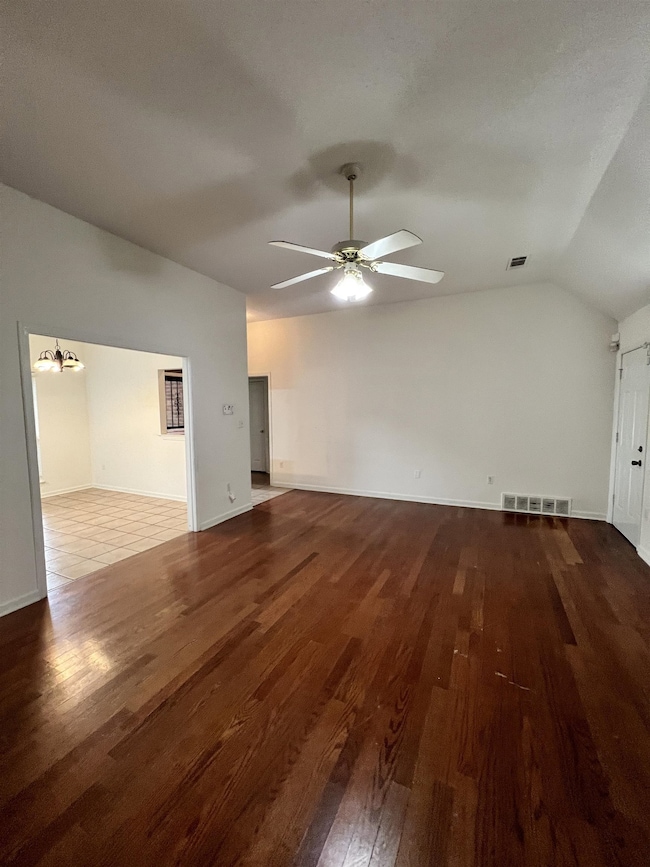 Unfurnished living room with dark wood-style flooring, lofted ceiling, a chandelier, and ceiling fan