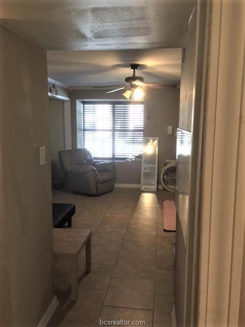 Tiled living area with a ceiling fan and baseboard