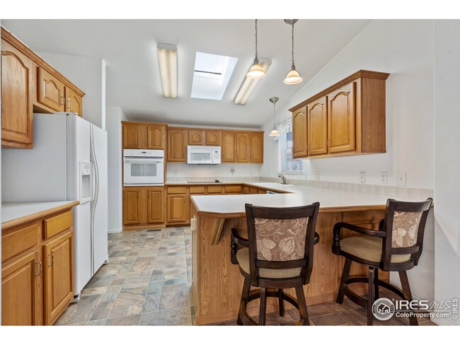 Large open kitchen with a huge skylight and 9ft+ ceilings, white appliances and breakfast nook seating.