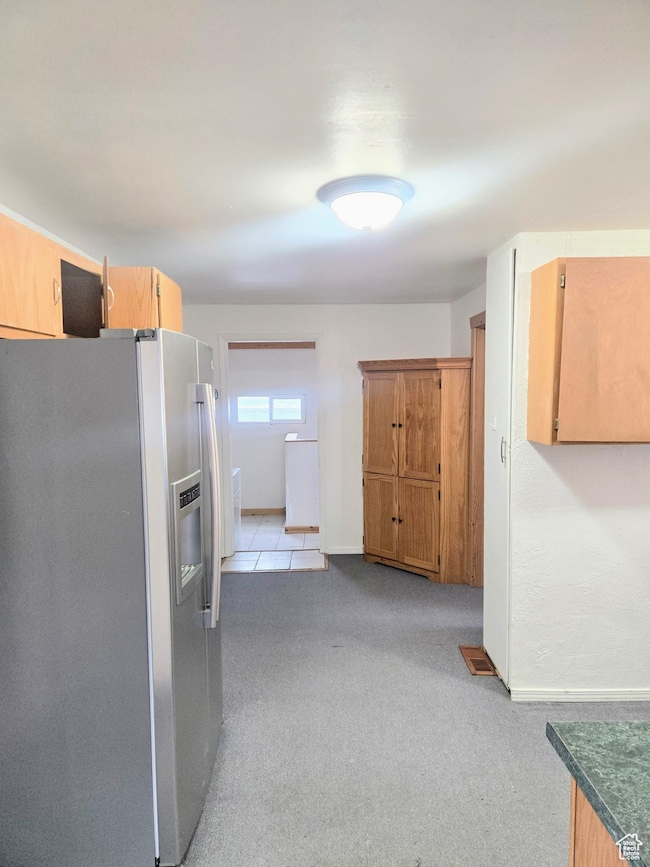 Kitchen with stainless steel fridge, light carpet, and brown cabinetry
