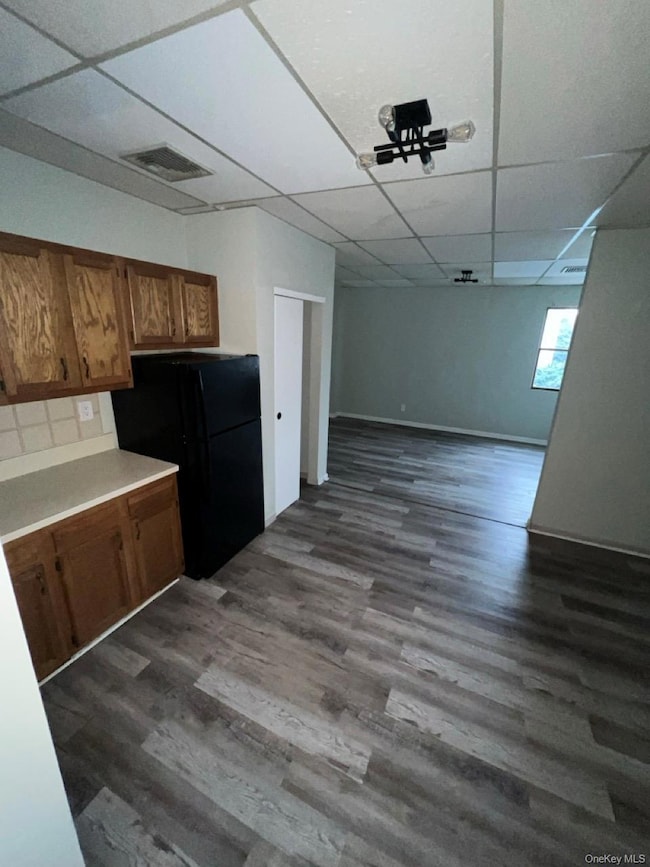 Kitchen featuring freestanding refrigerator, light countertops, brown cabinetry, dark wood-style flooring, and a paneled ceiling