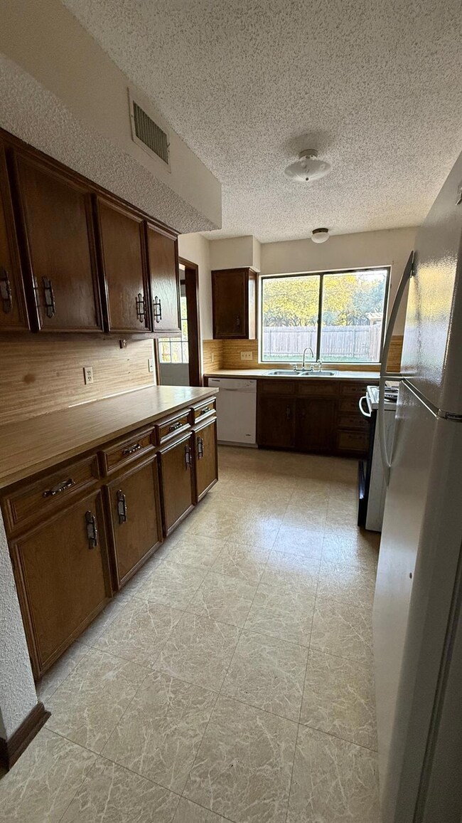 Kitchen featuring dark brown cabinetry, white appliances, light countertops, a textured ceiling, and light flooring