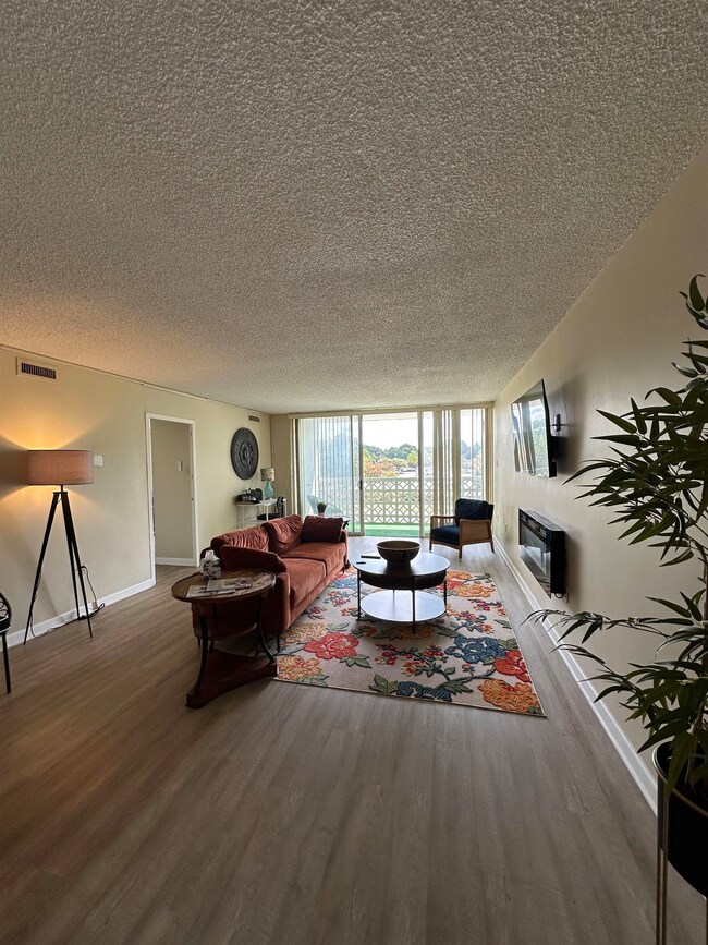Living room featuring floor to ceiling windows, a textured ceiling, wood finished floors, and a glass covered fireplace