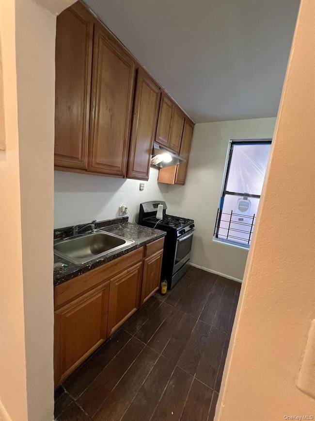 Kitchen with wood finish floors, stainless steel gas range, brown cabinetry, and under cabinet range hood