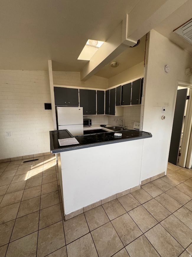 Kitchen featuring dark cabinets, decorative backsplash, freestanding refrigerator, a peninsula, and dark countertops