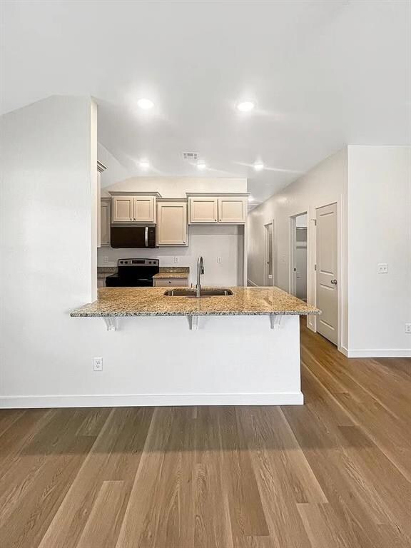 Kitchen with light stone countertops, stainless steel appliances, a peninsula, light wood-style floors, and recessed lighting.Note: Photos are of a similar home by the builder.