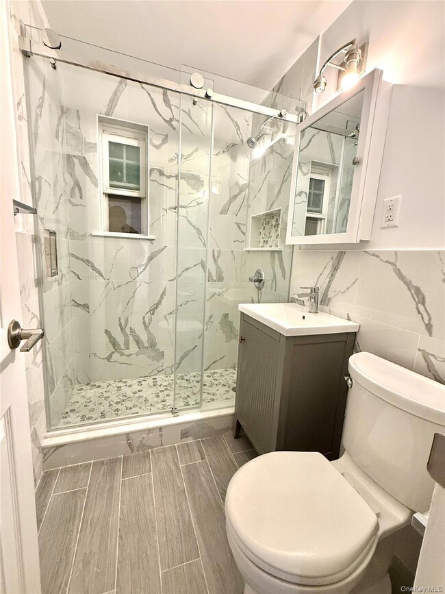 Bathroom with a marble finish shower, vanity, tile walls, and wood finish floors
